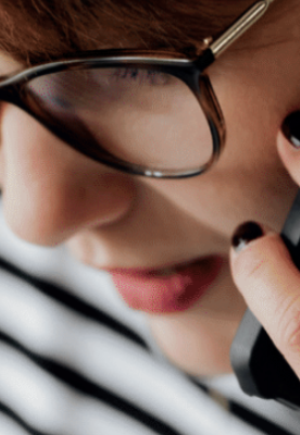 Eine Frau mit Brille und gestreiftem Hemd spricht am Handy